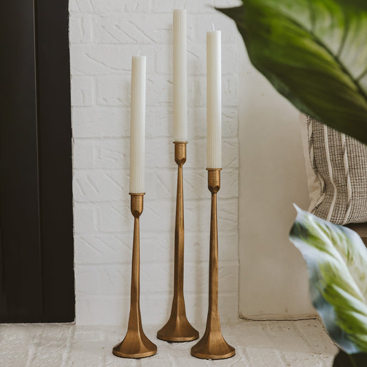 Three gold candle holders with white candles against a textured wall.