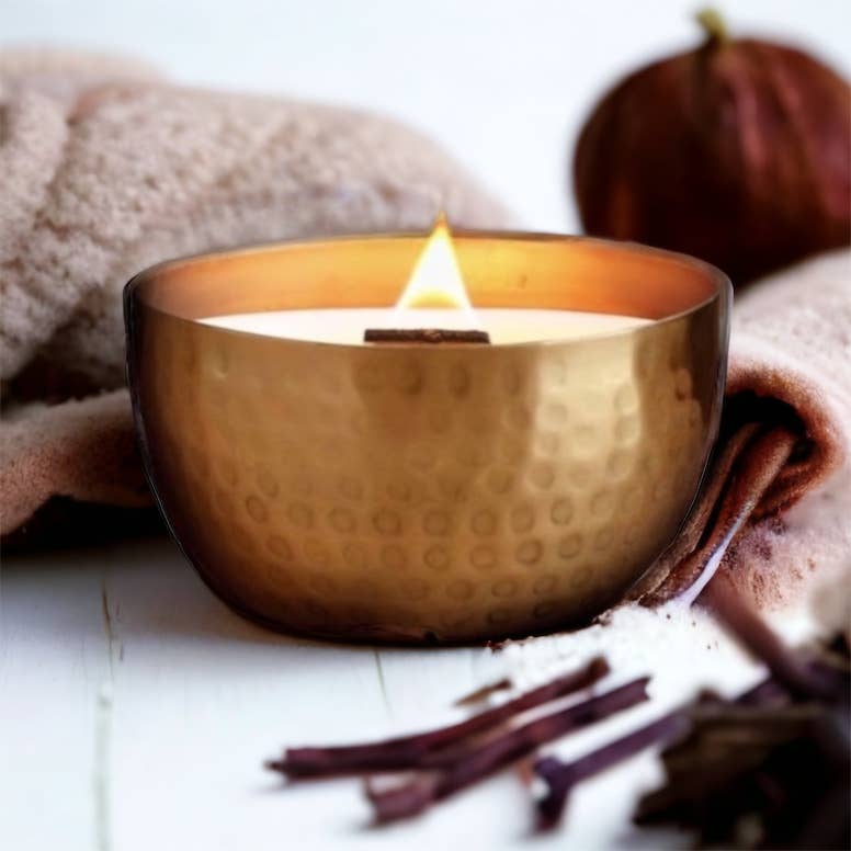 Cashmere Vanilla & Warm Amber – Solid Brass 14oz Pure Soy Candle - Gold candle holder with a lit candle on a white surface with cinnamon sticks and a towel.