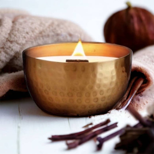Cashmere Vanilla & Warm Amber – Solid Brass 14oz Pure Soy Candle - Gold candle holder with a lit candle on a white surface with cinnamon sticks and a towel.