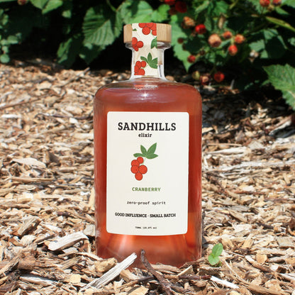 Bottle of Sandhills Elixir Cranberry on a wooden surface with greenery in the background