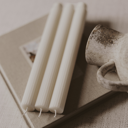 Three white candles on a textured surface with a ceramic mug in the background